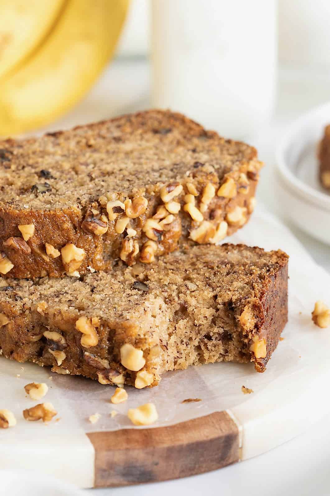 Two slices of banana nut bread on a white marble counter. One slice has a bite out of it.