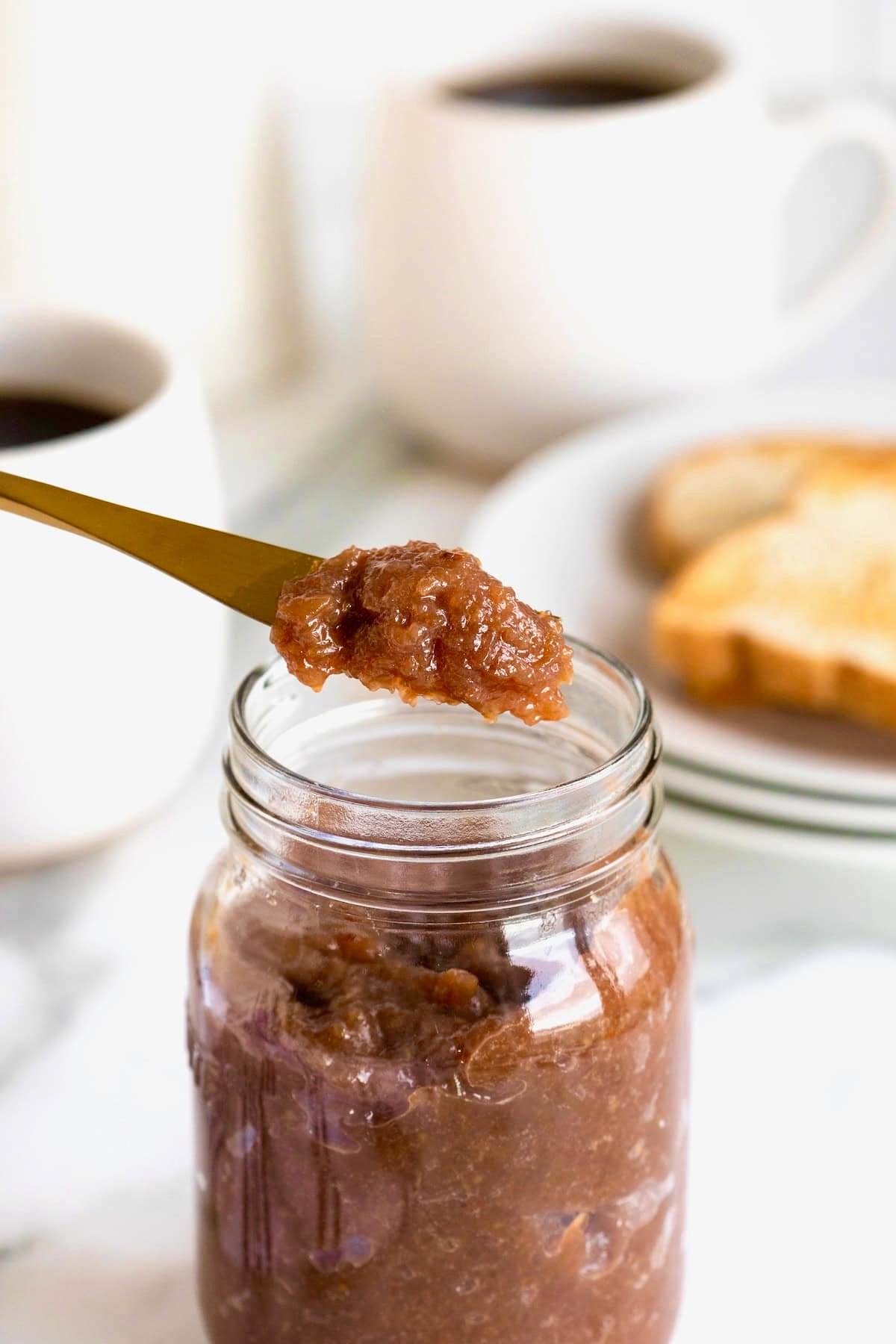 A spoonful of grape jam over a jar of homemade grape jam.