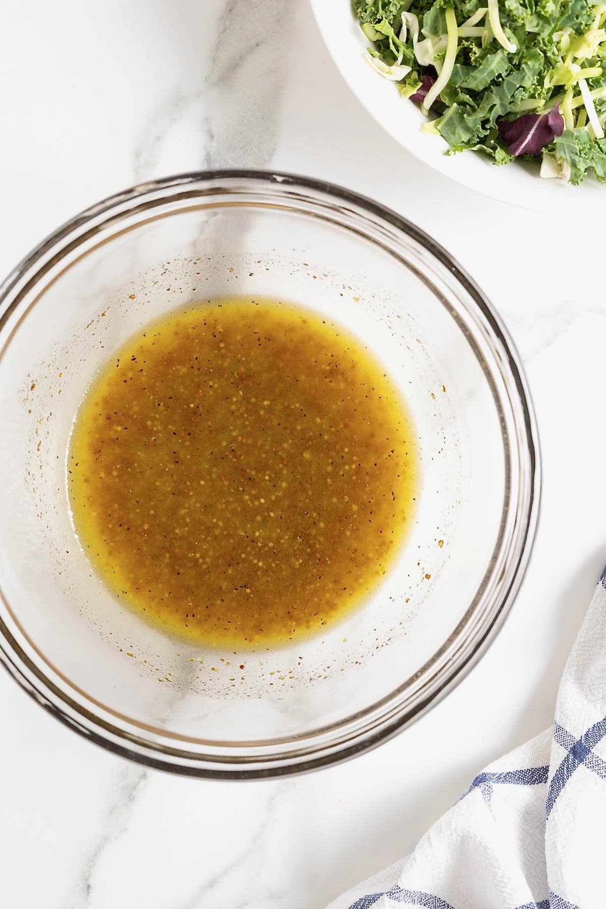 A glass mixing bowl of salad dressing on white marble counter.