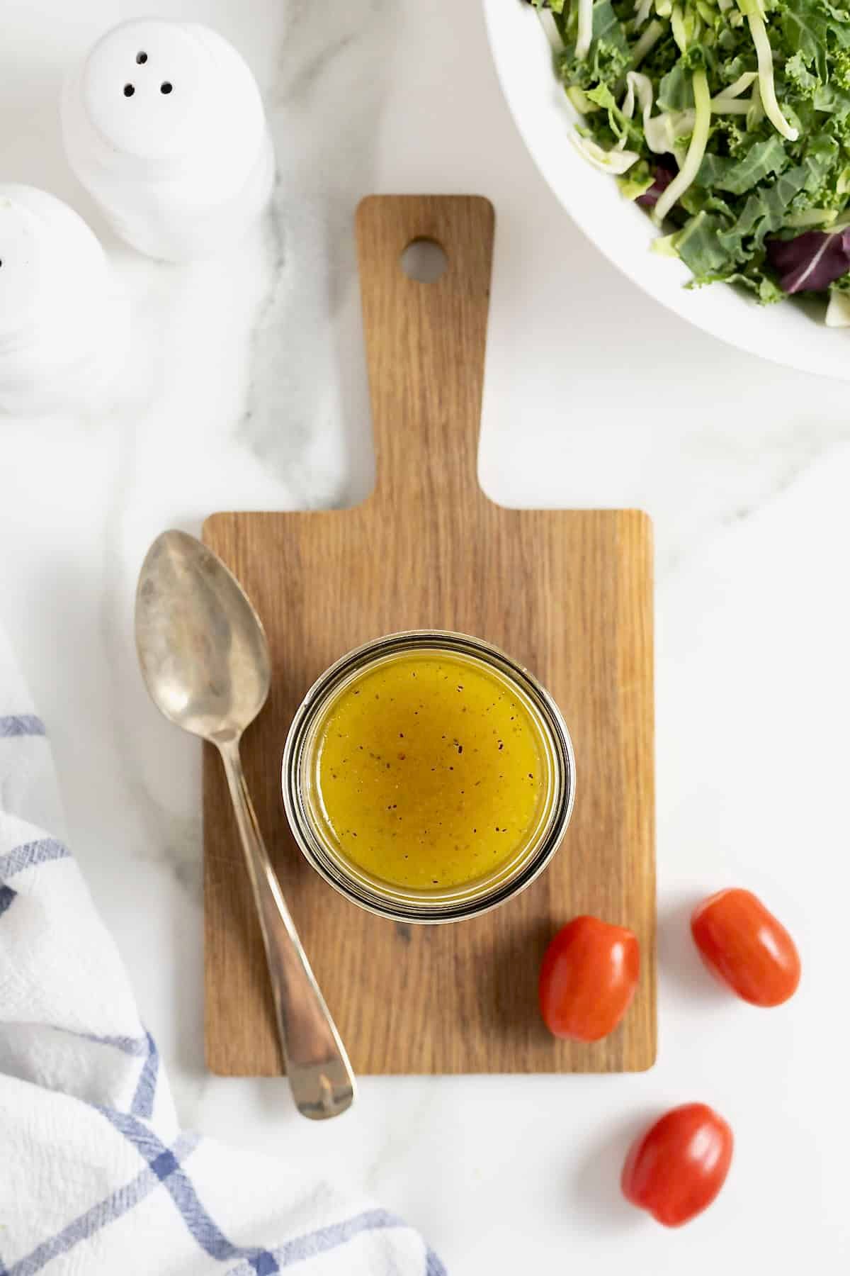 A jar of salad dressing on a rectangular wood cutting board on a white marble counter.