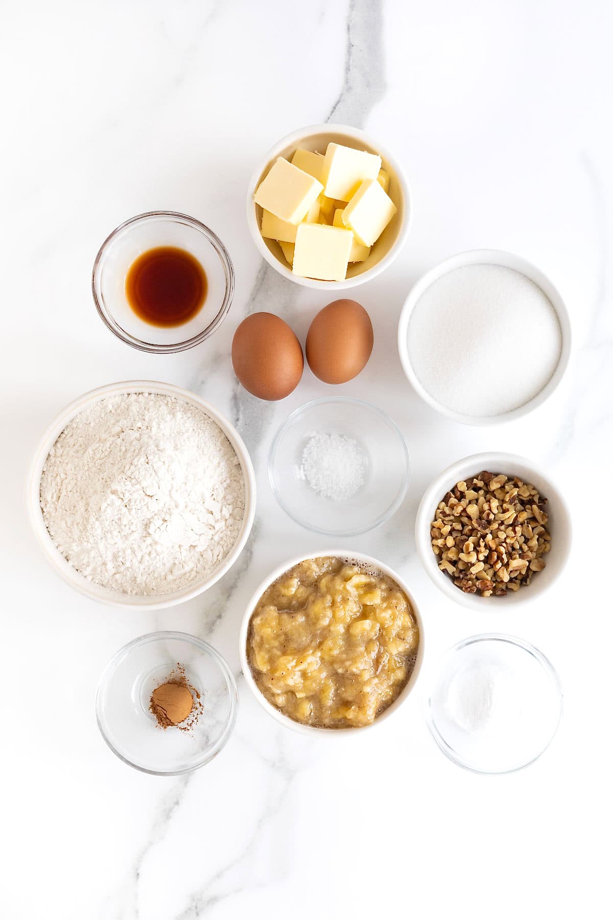 Ingredients to make brown butter banana nut bread in small white dishes on a white marble counter.