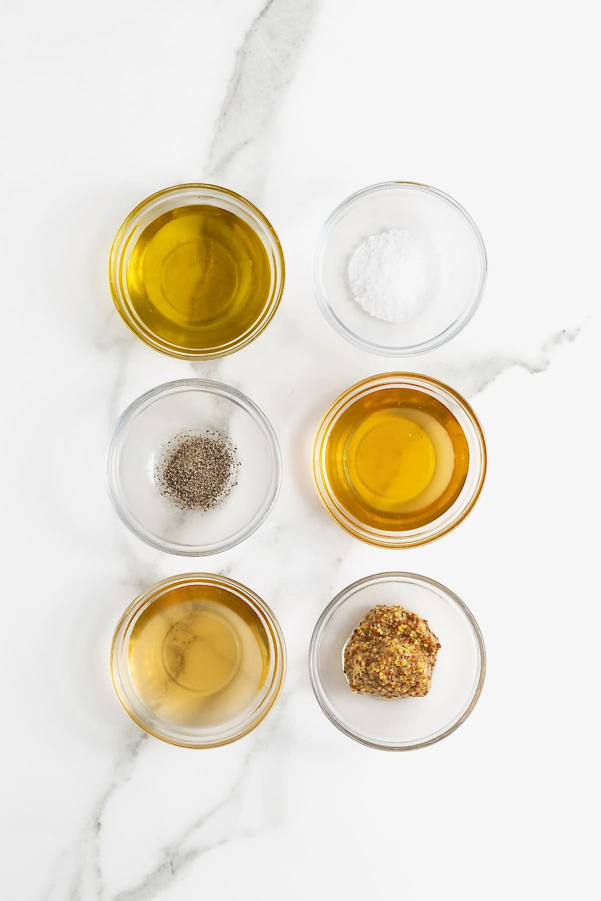 Ingredients to make champagne vinaigrette in small glass dishes on a white marble counter.