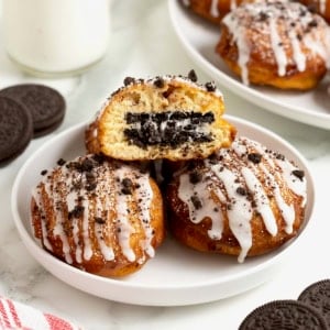 A white rimmed plate holding three fried cinnamon rolls with Oreos in the middle. The one of top is cut open to reveal the Oreo inside.