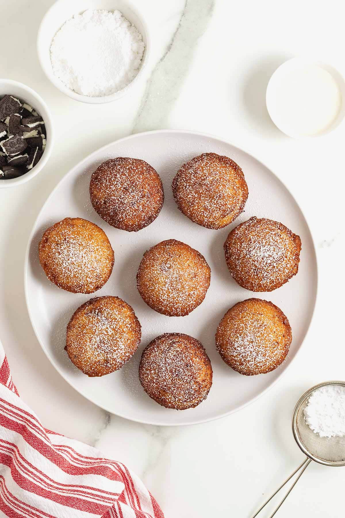 A white rimmed plate filled with 8 cinnamon roll fried Oreos dusted with powdered sugar.