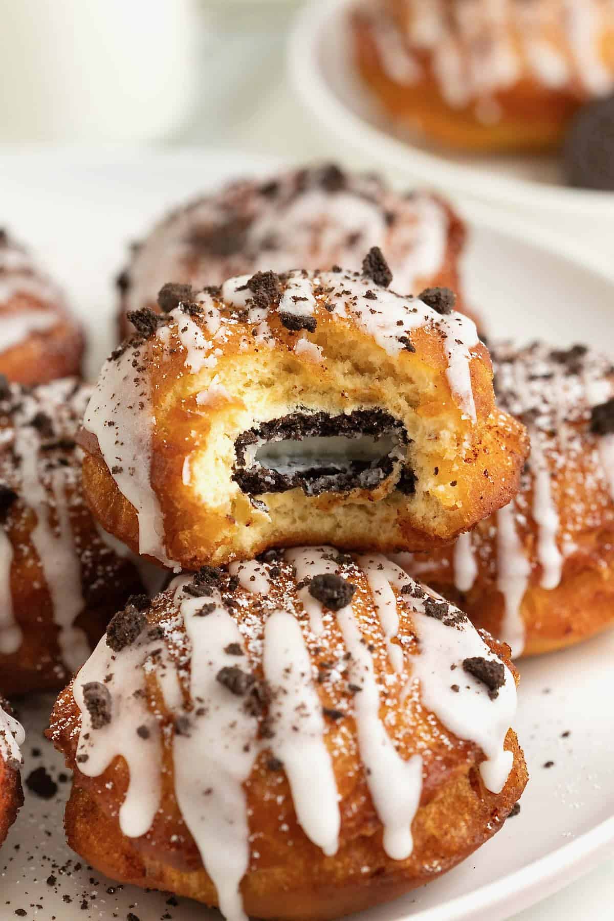 A white rimmed plate holding three fried cinnamon rolls with Oreos in the middle. The one of top is cut open to reveal the Oreo cookie inside.