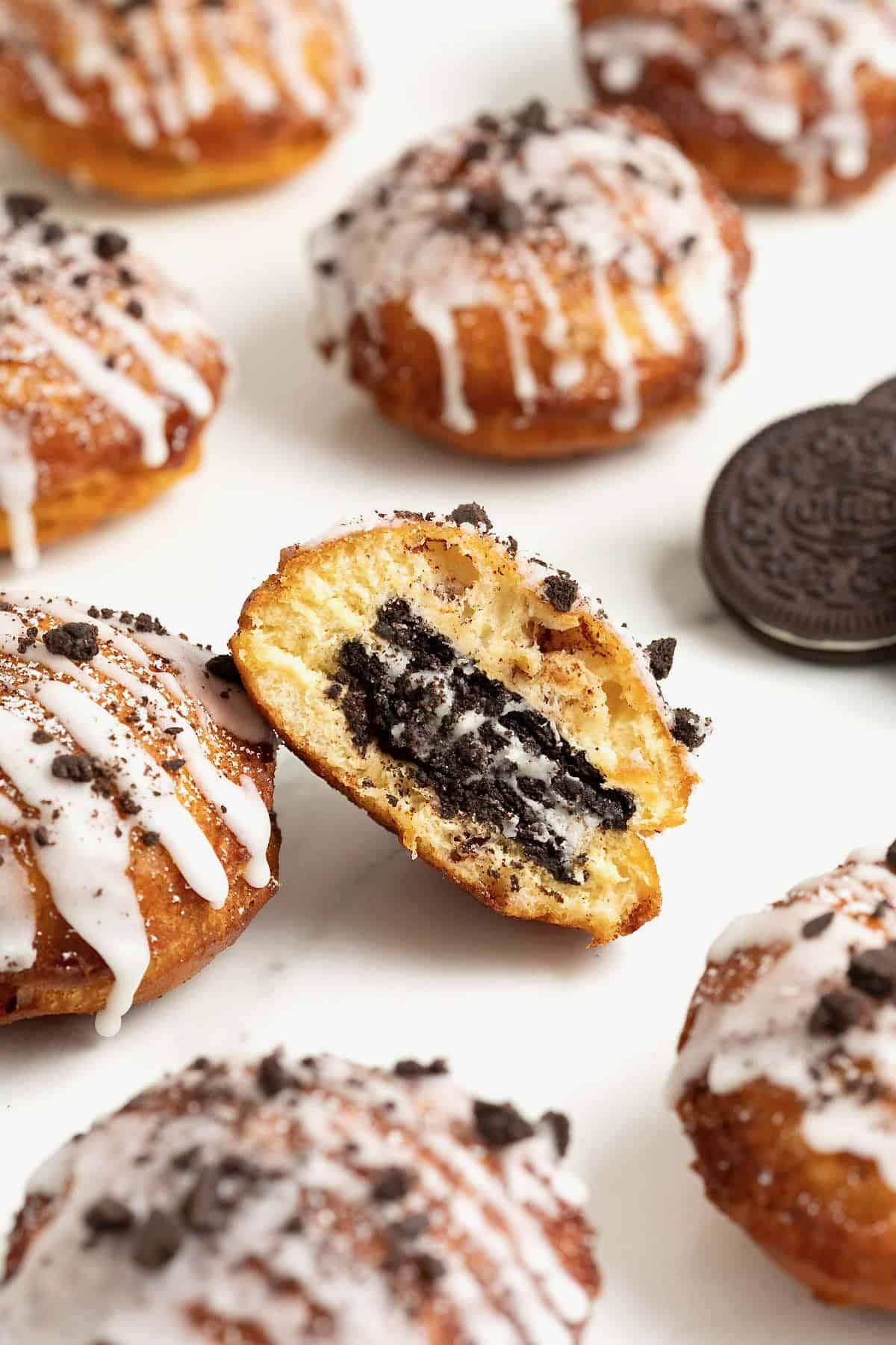 Six cinnamon roll fried Oreos on a white marble counter. The center one is cut in half to show the Oreo inside.