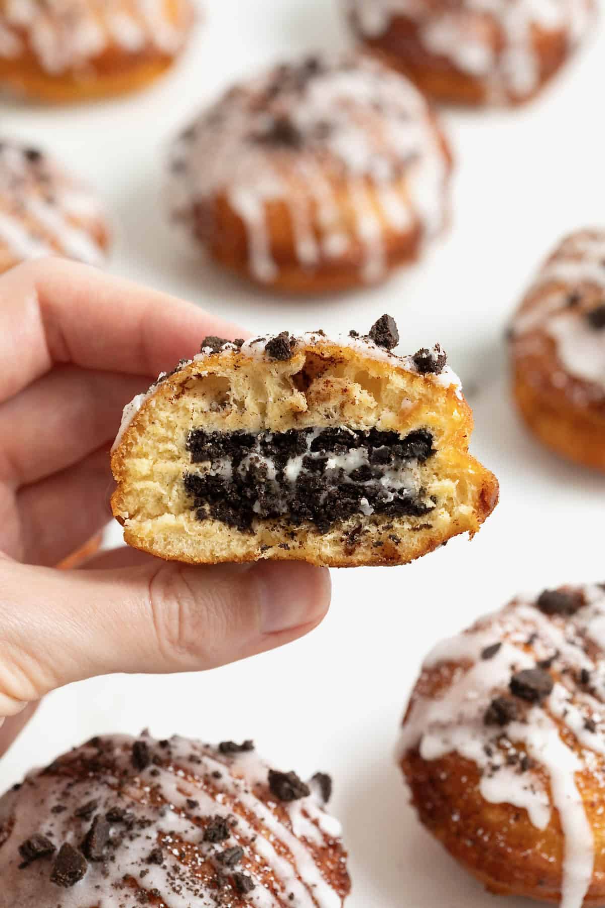 A hand holding a cinnamon roll fried Oreo with a bite out of it.