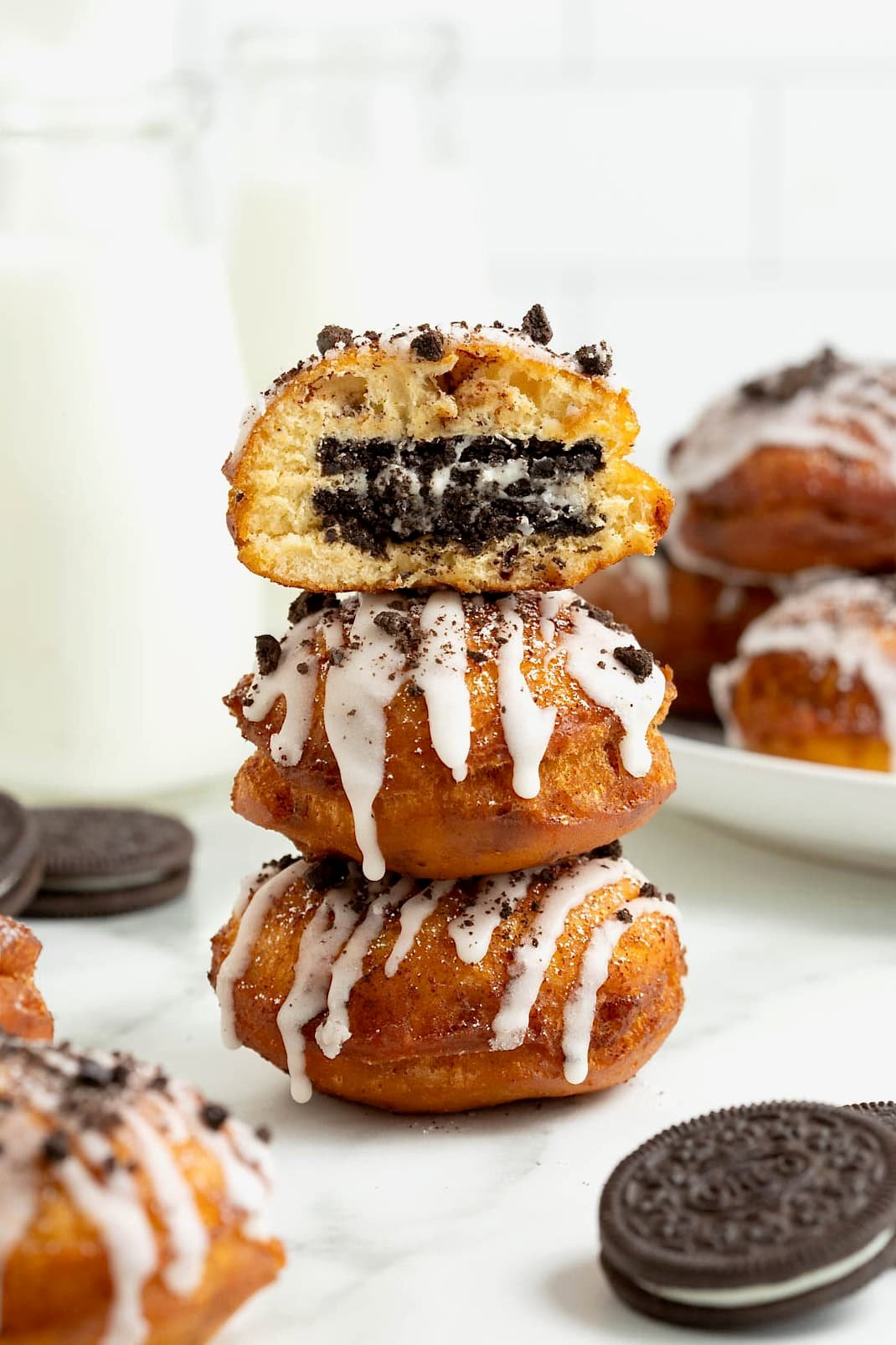 A stack of three cinnamon roll fried Oreos on a white marble counter. The top fried Oreo has a bite out of it revealing the Oreo inside.