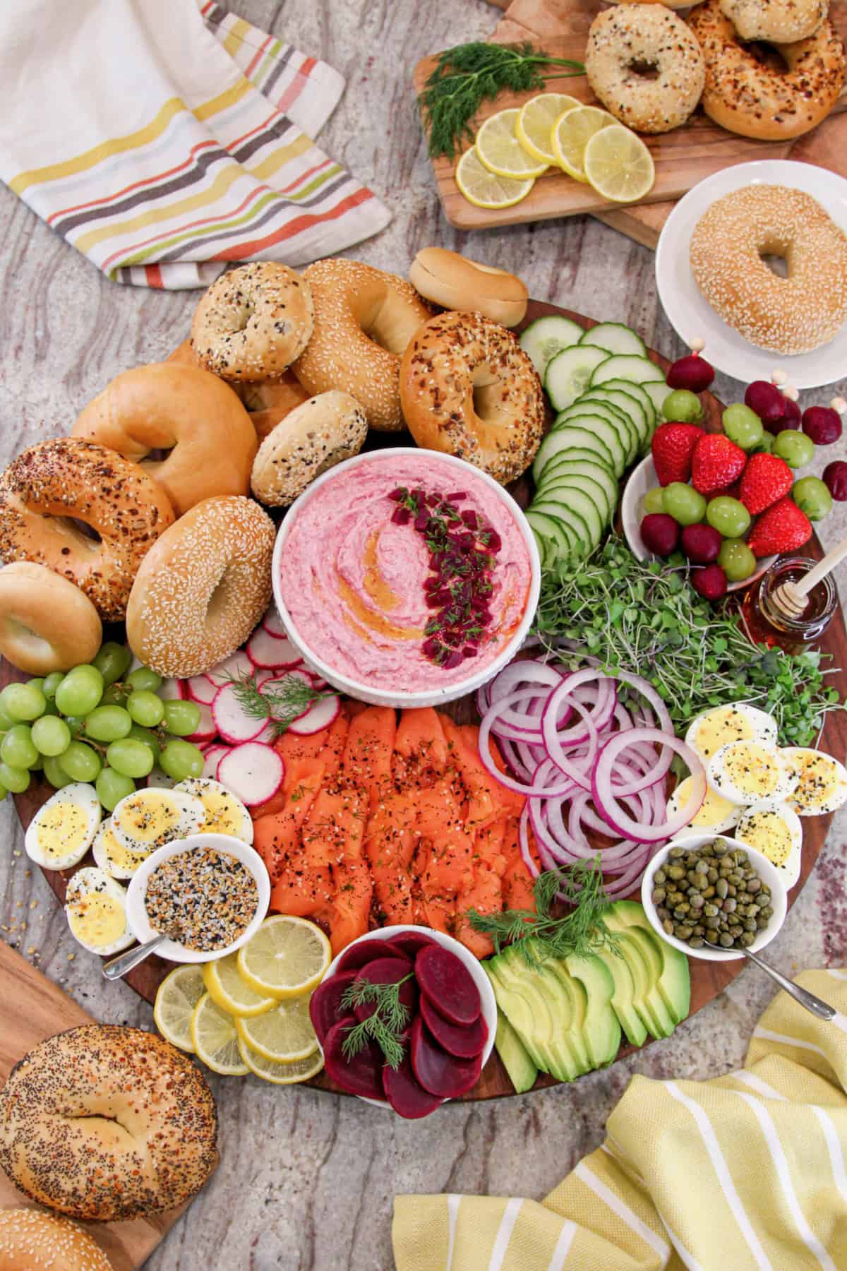 A large round wood board with fixings to make bagel breakfast sandwiches and a white bowl of beet cream cheese in the middle.