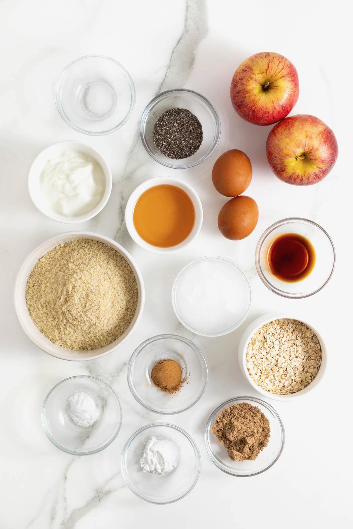 Ingredients to make superfood muffins in small glass dishes on a white marble counter.