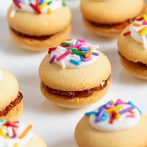 Eight vanilla wafer sandwich cookies topped with white icing and confetti sprinkles on a parchment surface.