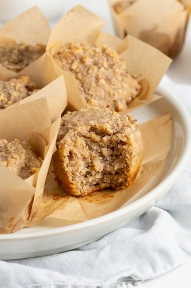 A white plate of tan muffins in brown paper muffin wrappers.