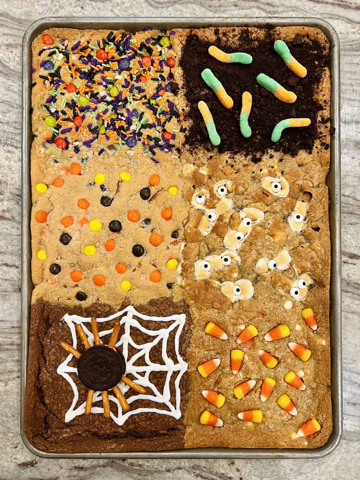 Halloween cookie bars in a sheet pan on a gray and white marble counter.