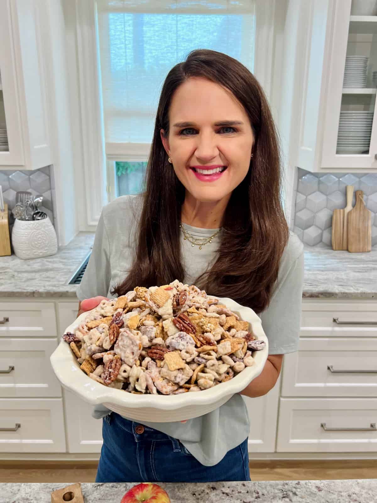 Maegan Brown holding a white scalloped bowl of Apple Pie Snack Mix.