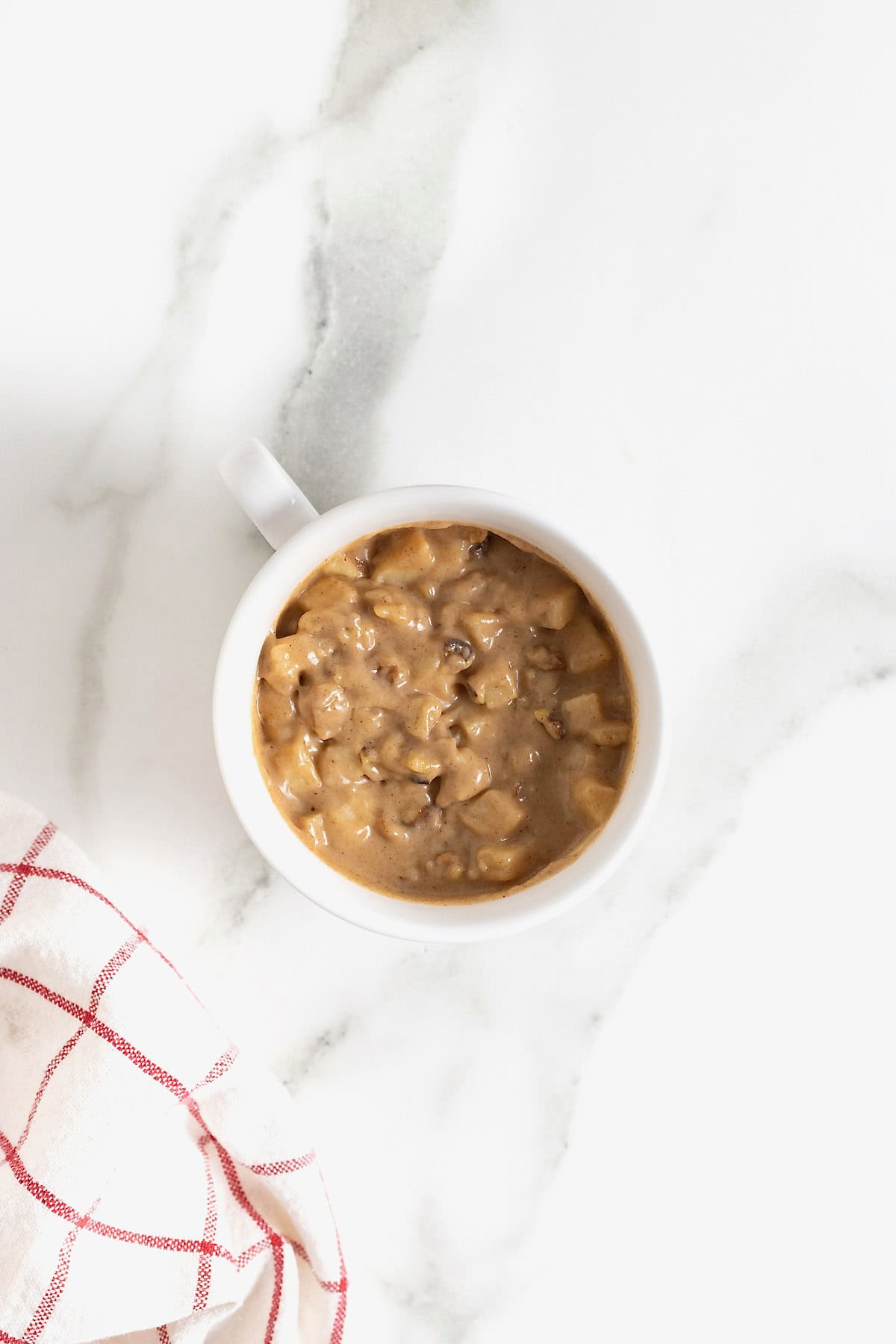 Apple cake batter in a white mug on a white marble counter.
