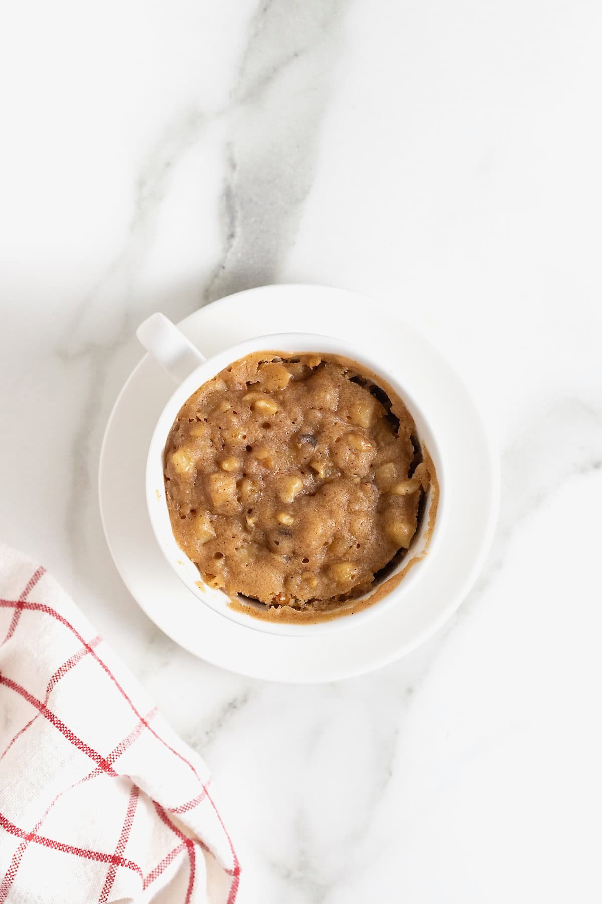 A microwave apple cake in a white mug on a white marble counter.
