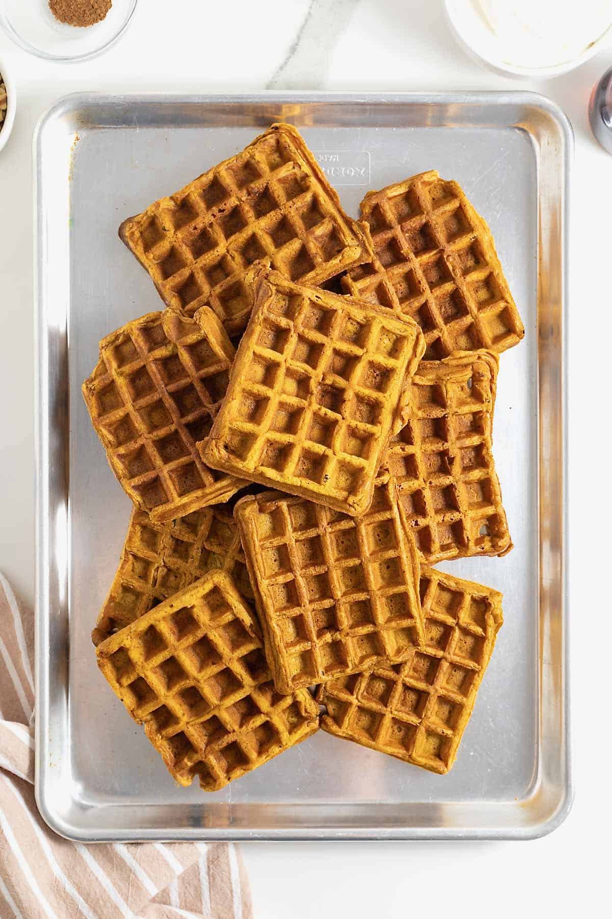 Pumpkin waffles piled on an aluminum baking sheet.