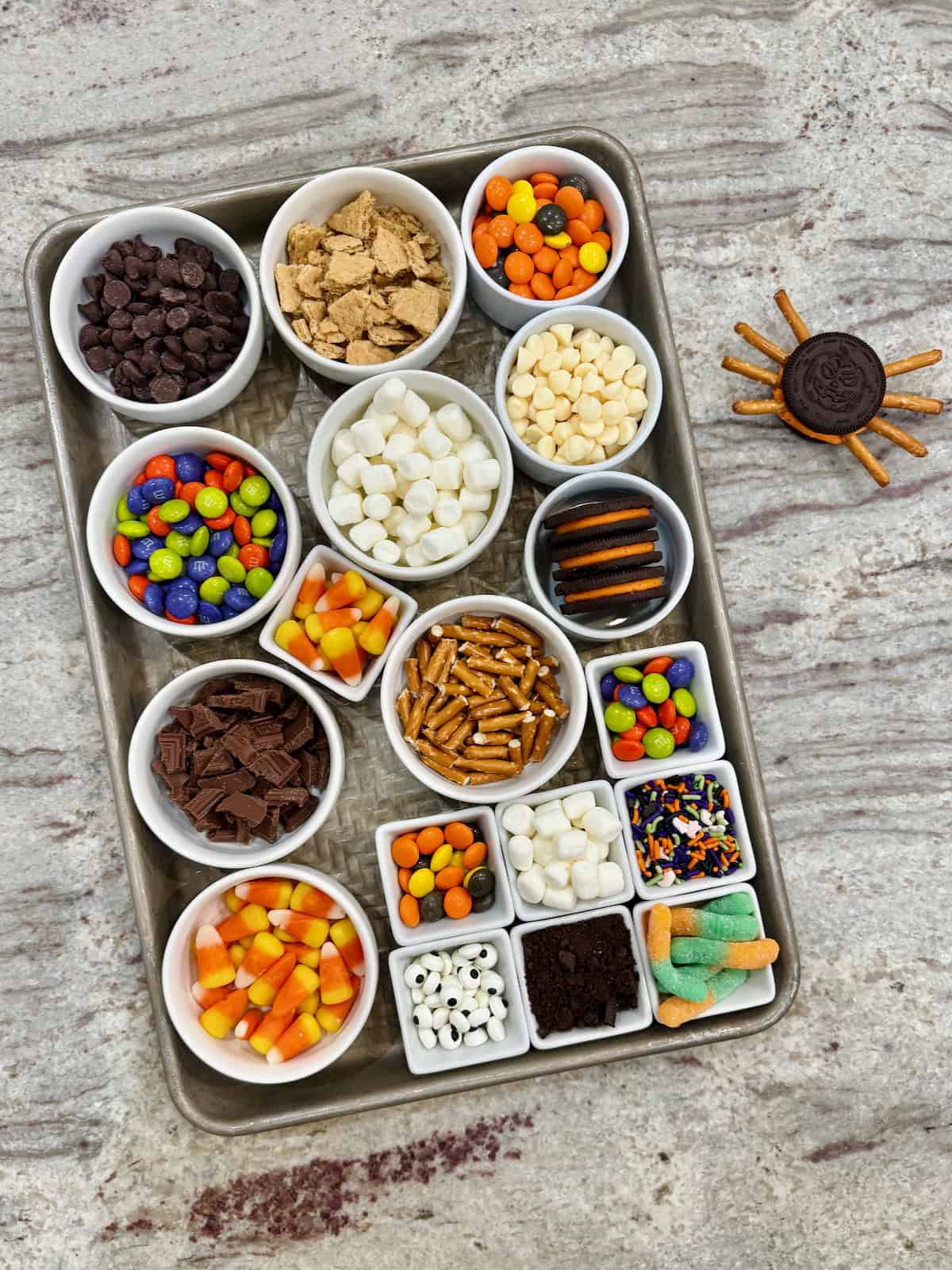 Ingredients to make Halloween Cookie Bars in small glass dishes in a rimmed backing sheet.