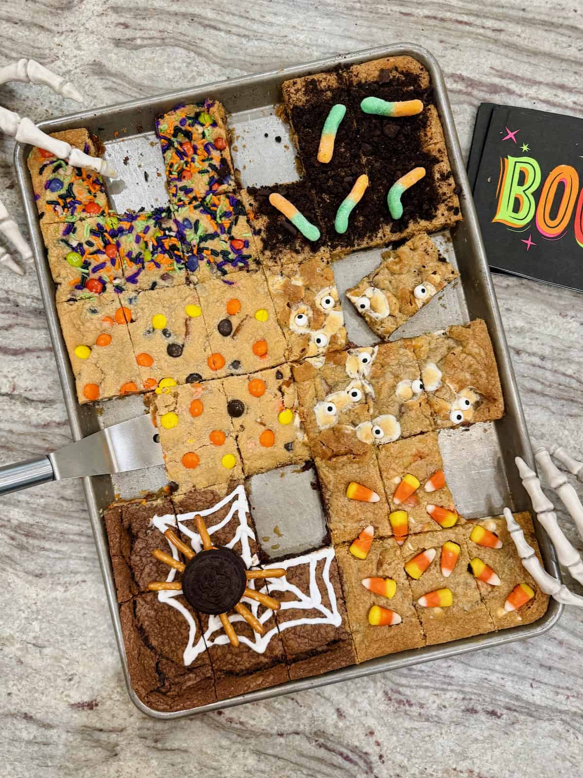 Halloween cookie bars in a sheet pan on a gray and white marble counter.