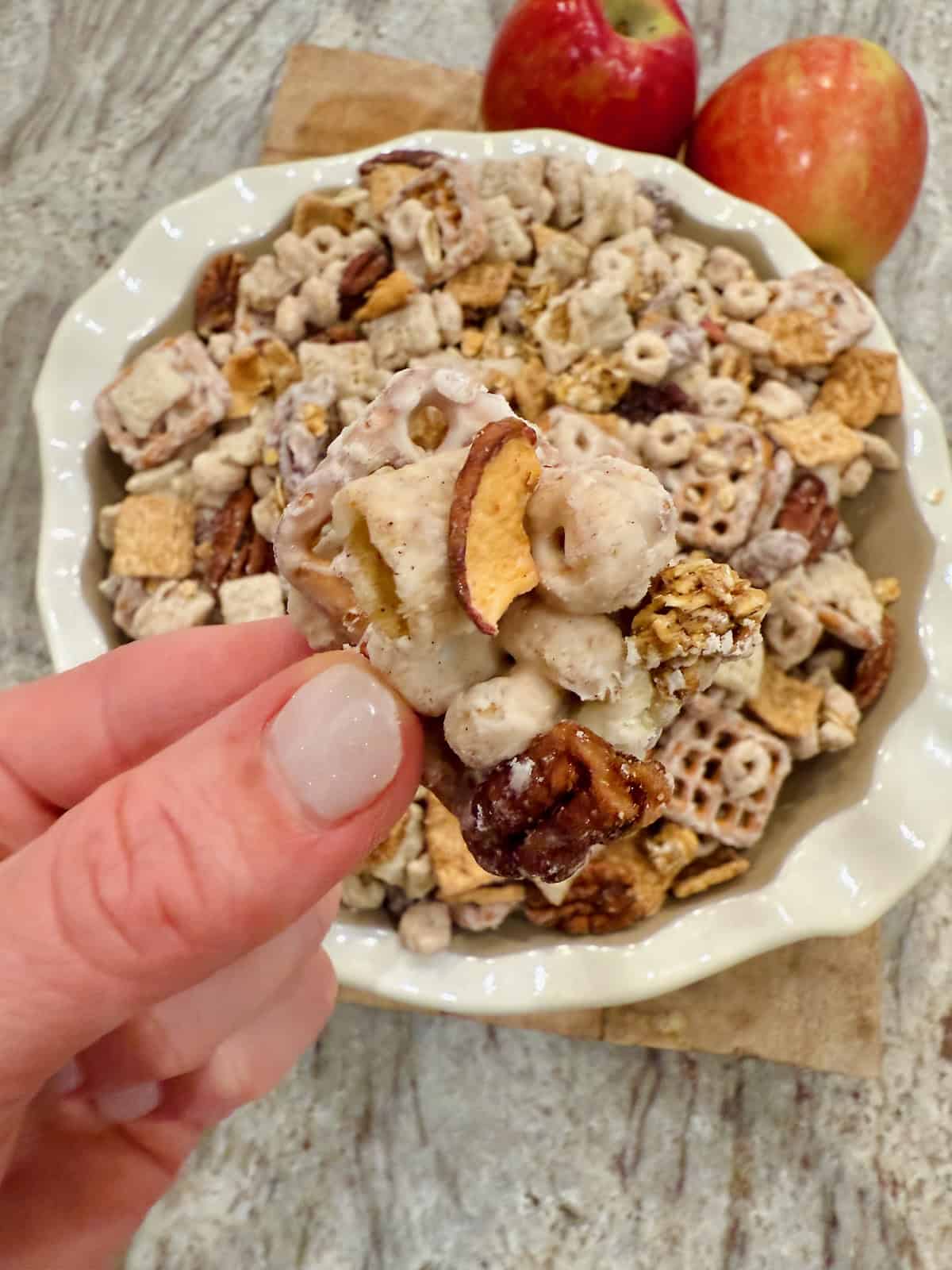 A cluster of Apple Pie Snack Mix between two fingers.