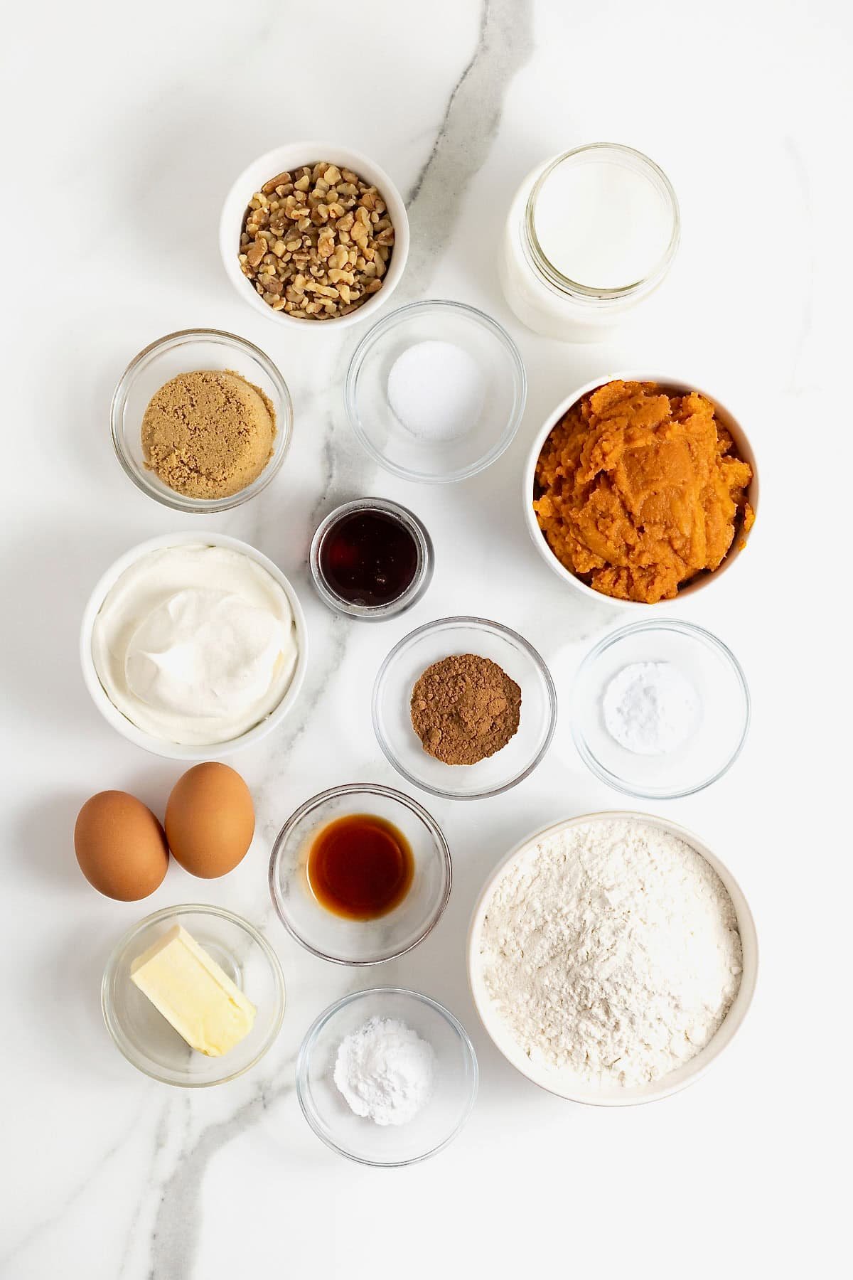 Ingredients to make Pumpkin Waffles in small glass dishes on a white marble counter.