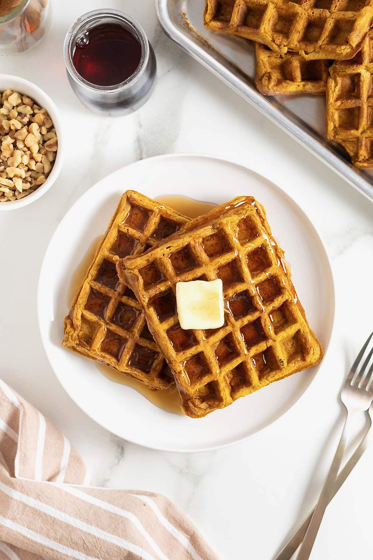 Two pumpkin waffles laying overlapping on a white plate. There is a square of butter on the top waffle.
