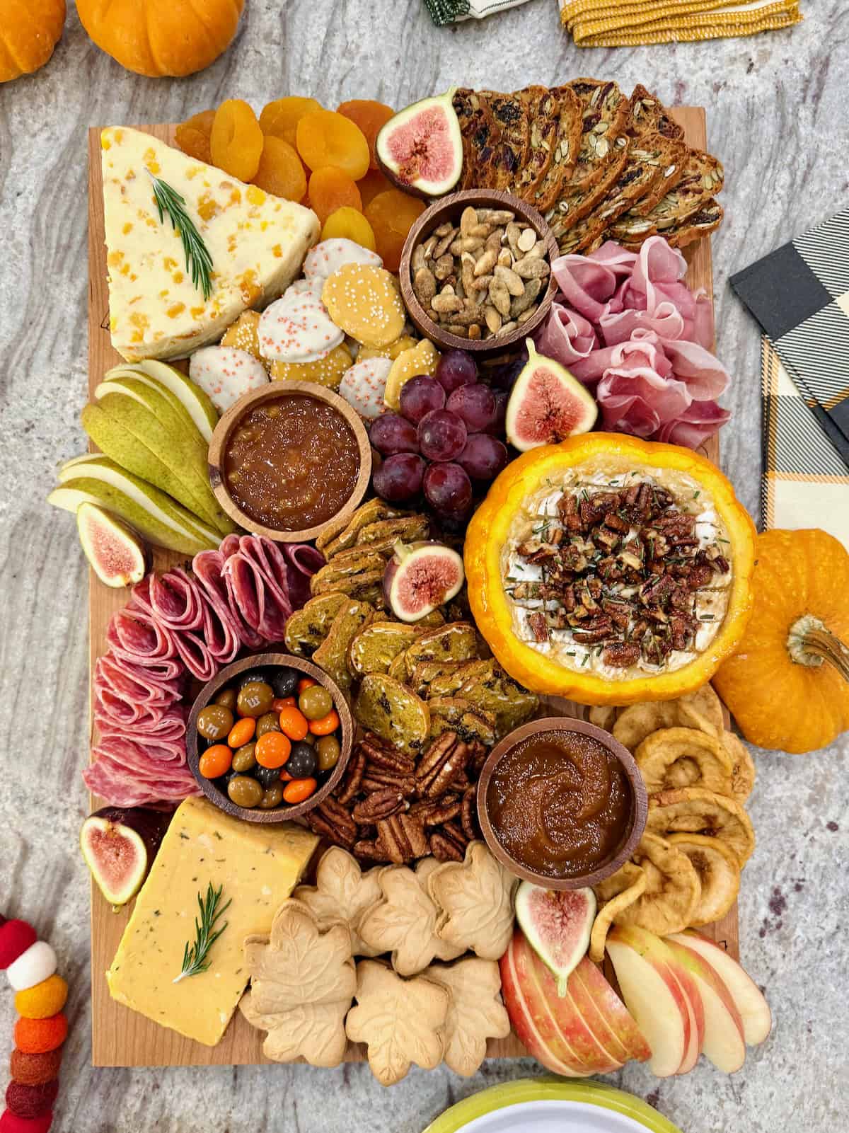 A rectangular wooden food board filled with autumnal snacks like cheese, salami, sliced pear and a pumpkin dip.