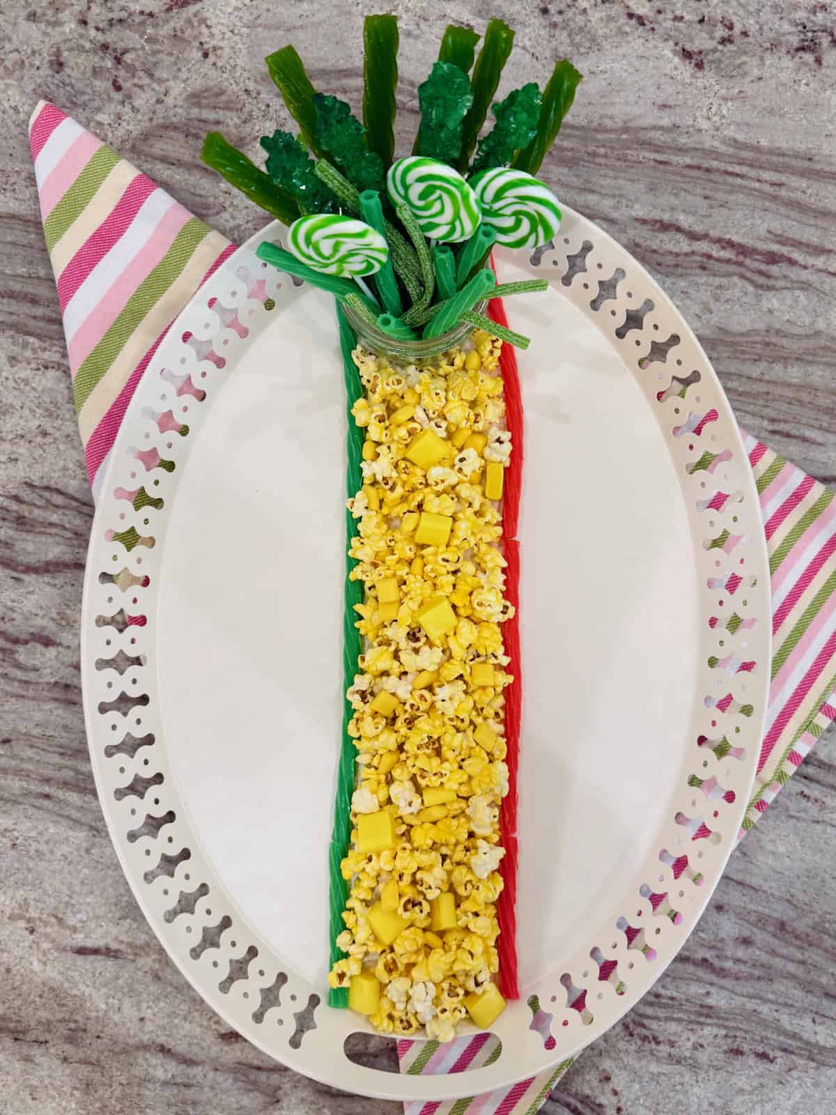An oblong serving tray with a yellow column of popcorn down the middle and a jar of green treats in the 12 o'clock position.