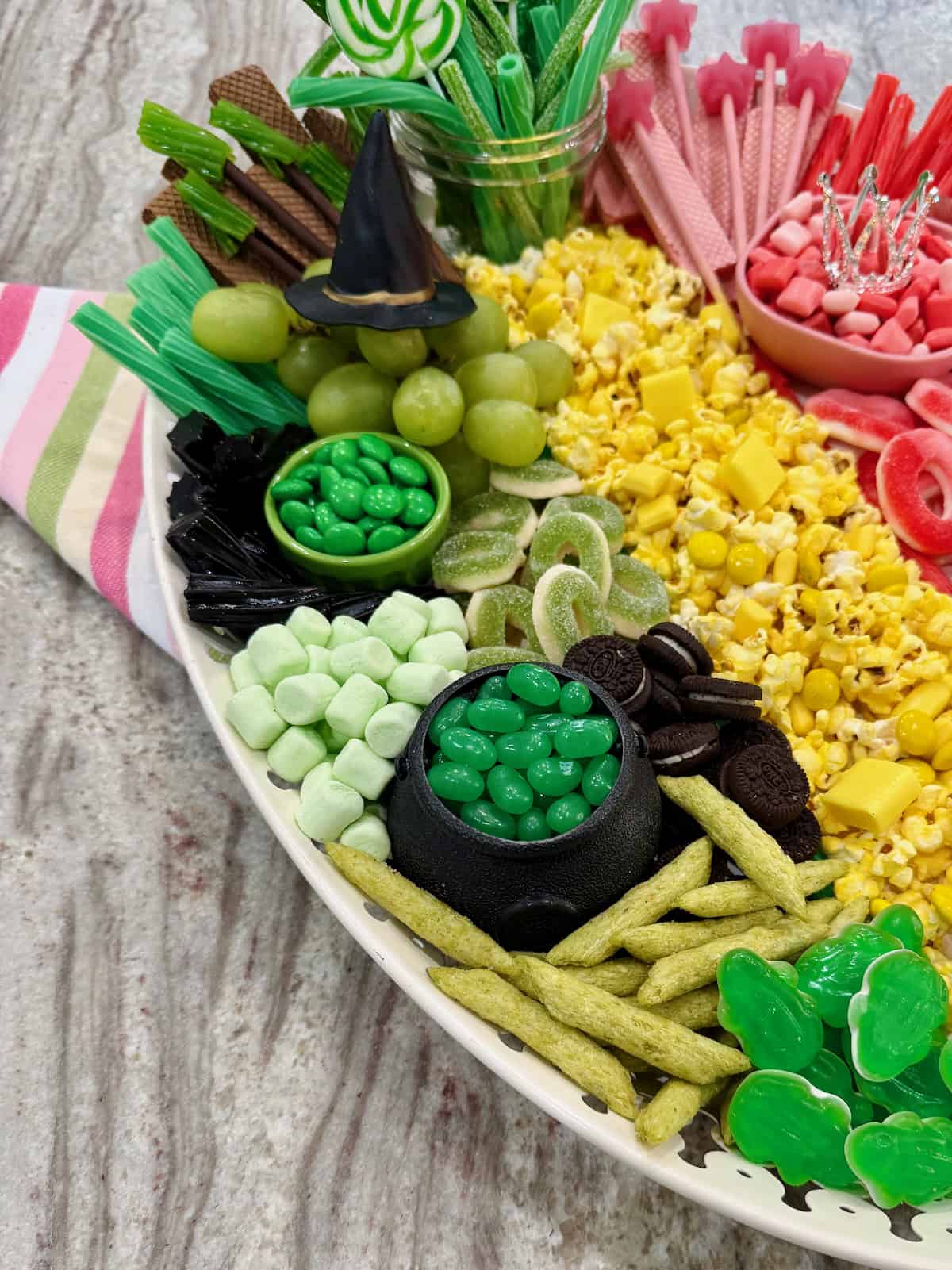Green candies, grapes, black licorice and wafter cookies on the left side of an oblong white serving tray.