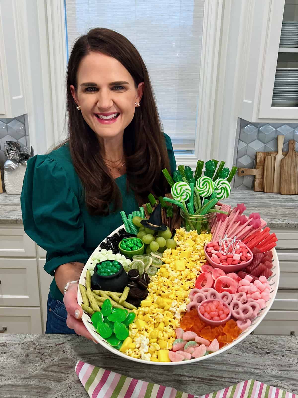 Maegan brown wearing a dark green sweater holding the Wicked Movie Snack Board.