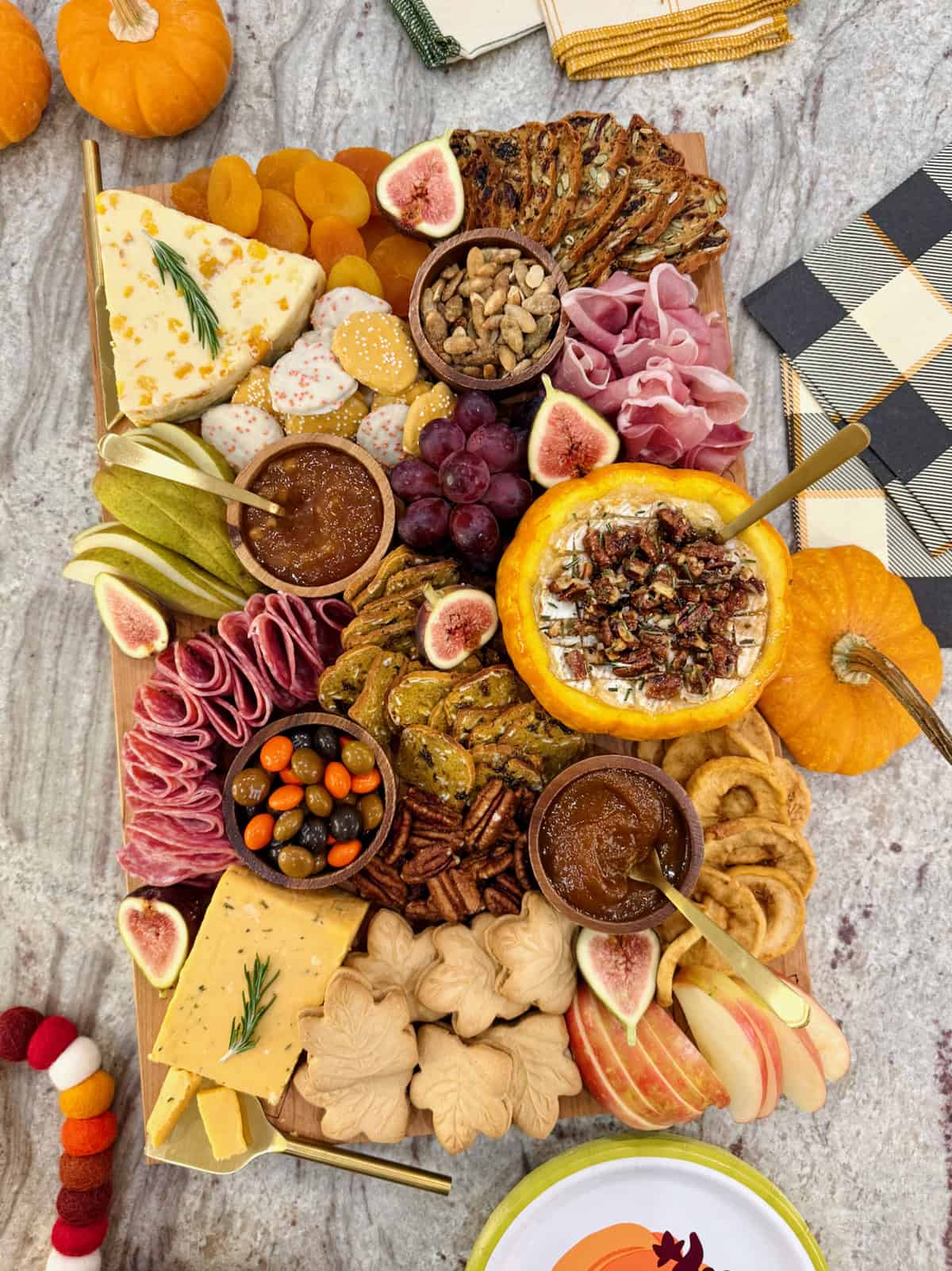 A rectangular wooden food board filled with autumnal snacks like cheese, salami, sliced pear and a pumpkin dip.
