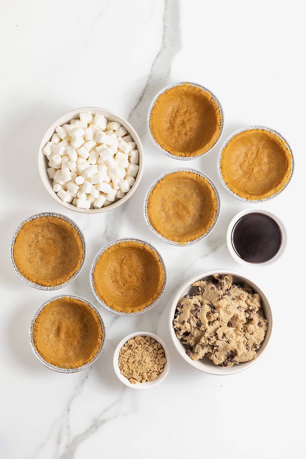 Ingredients to make mini s'mores cookie pies on a white marble counter. 