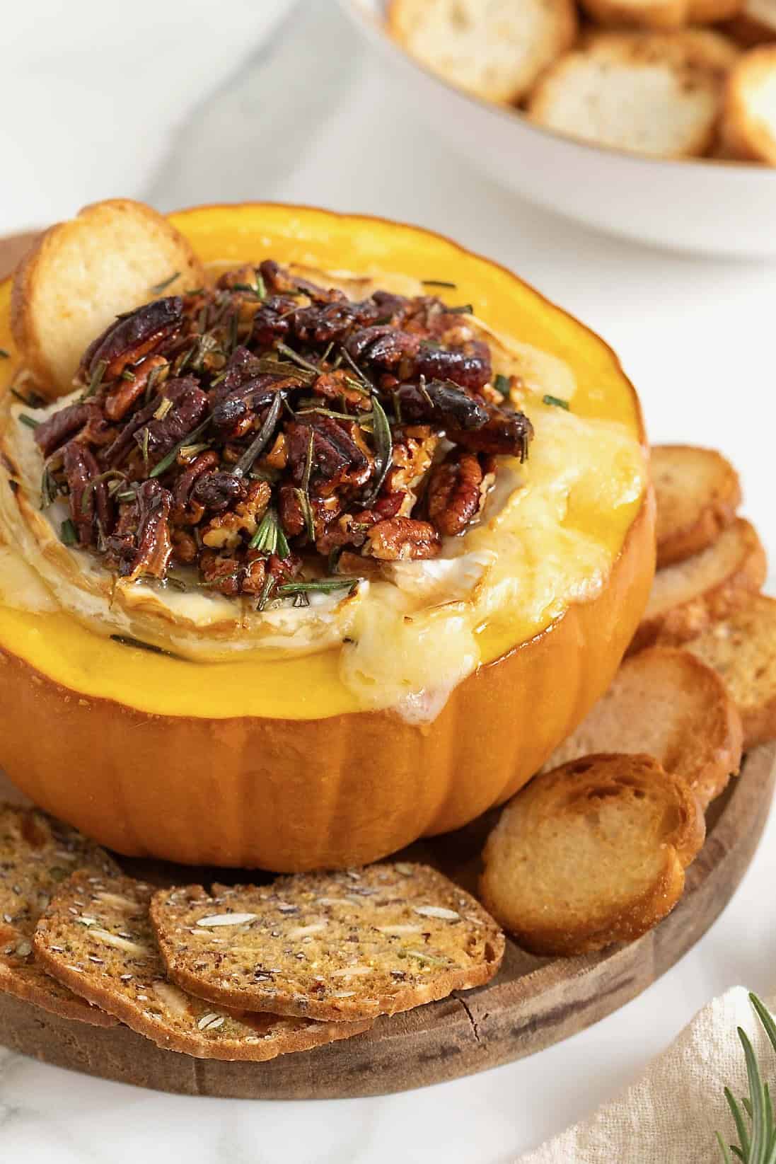 Baked brie in a hollowed out mini pumpkin topped with chopped pecans and rosemary.