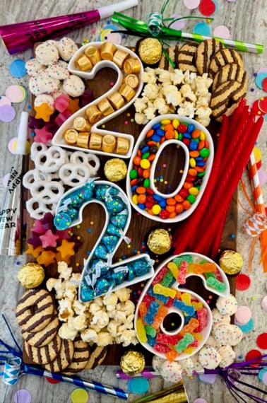a rectangular walnut food board filled with sweets in number containers that spell out 2026.