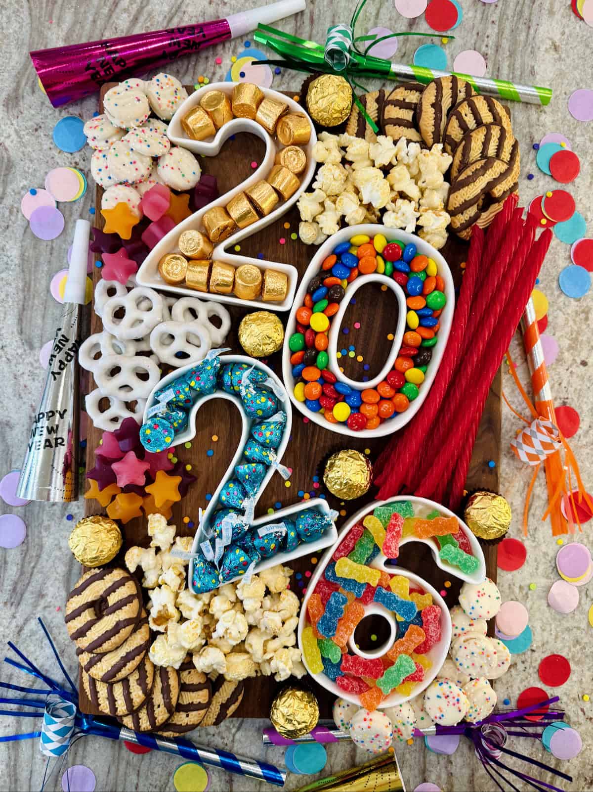 a rectangular walnut food board filled with sweets in number containers that spell out 2026.