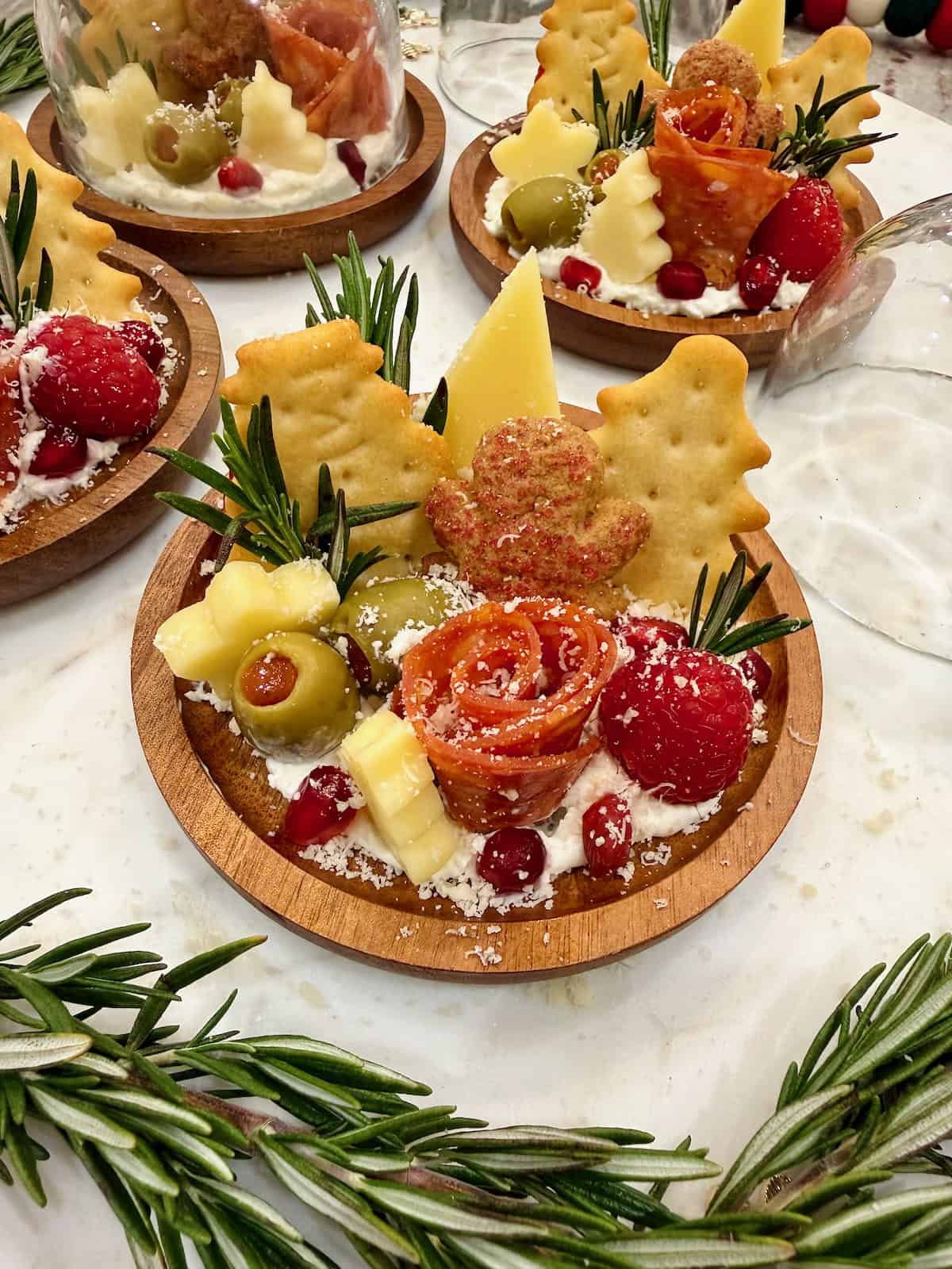 Four small round charcuterie boards feature a salami rose, star cheese and Christmas tree shaped crackers.