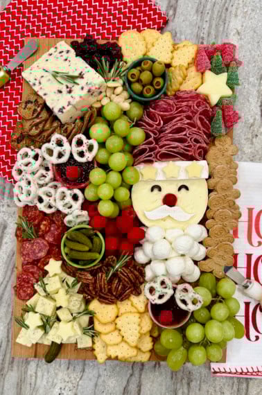 A Christmas charcuterie board with a Santa made out of salami and cheeses, as well as other festive touches.
