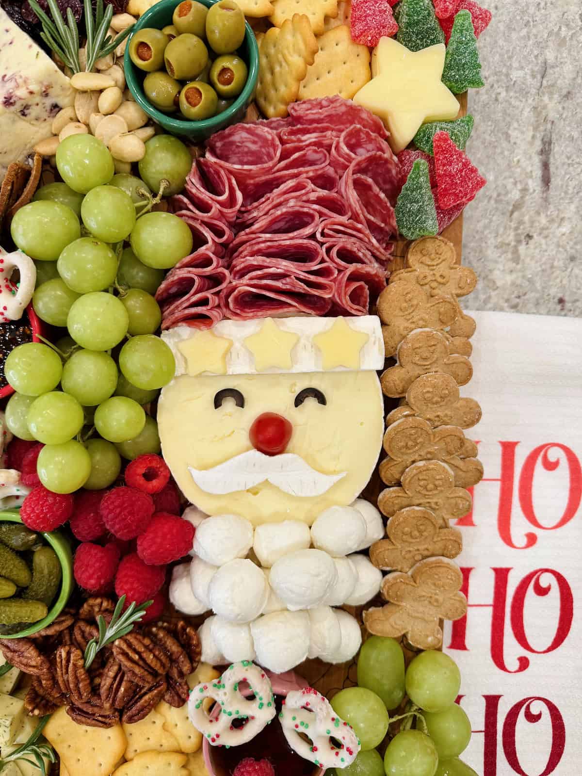 Grapes, Christmas tree shaped crackers, pecan halves and Christmas chocolate covered pretzels on a food board.