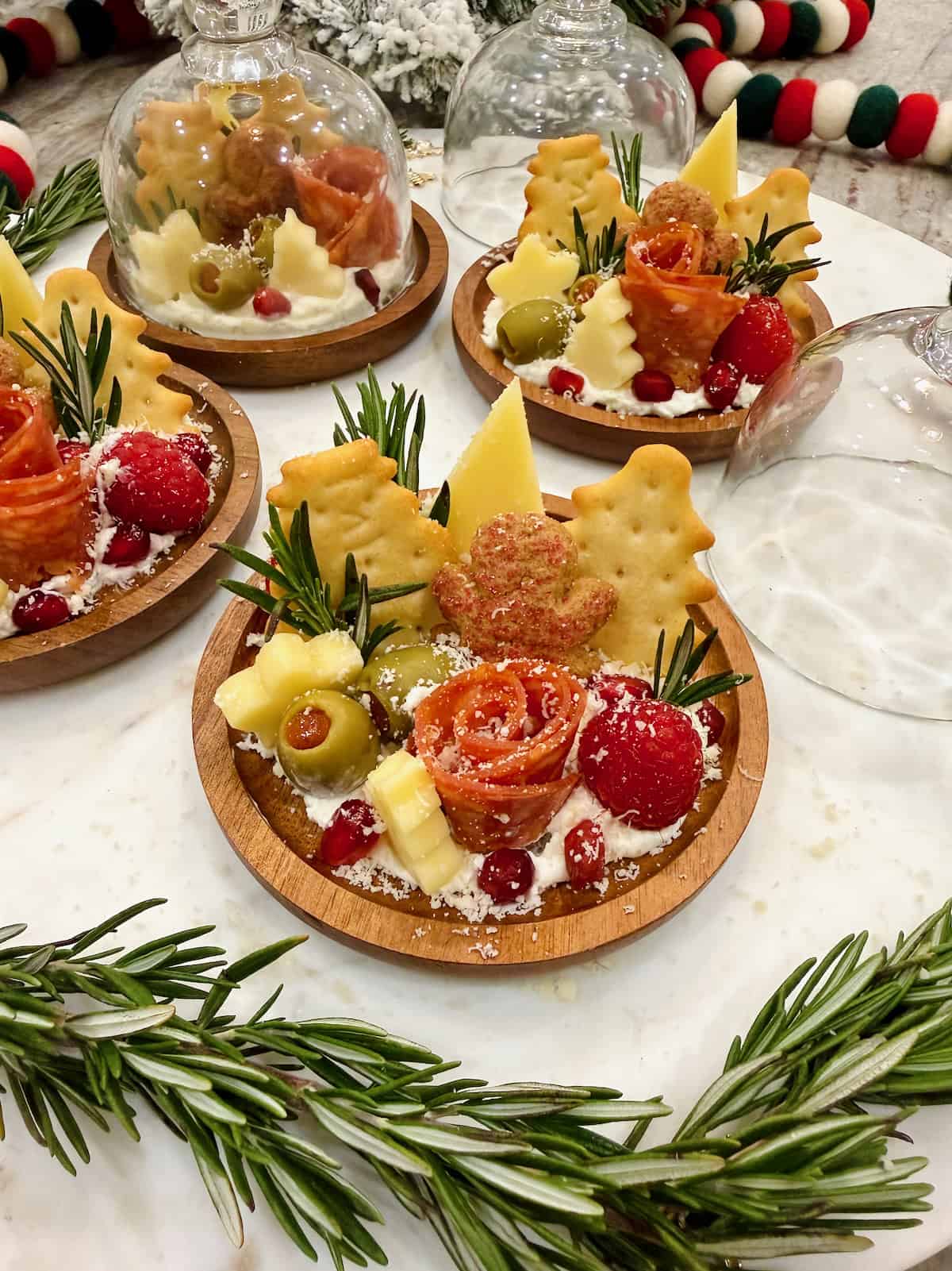 Four small round charcuterie boards feature a salami rose, star cheese and Christmas tree shaped crackers.