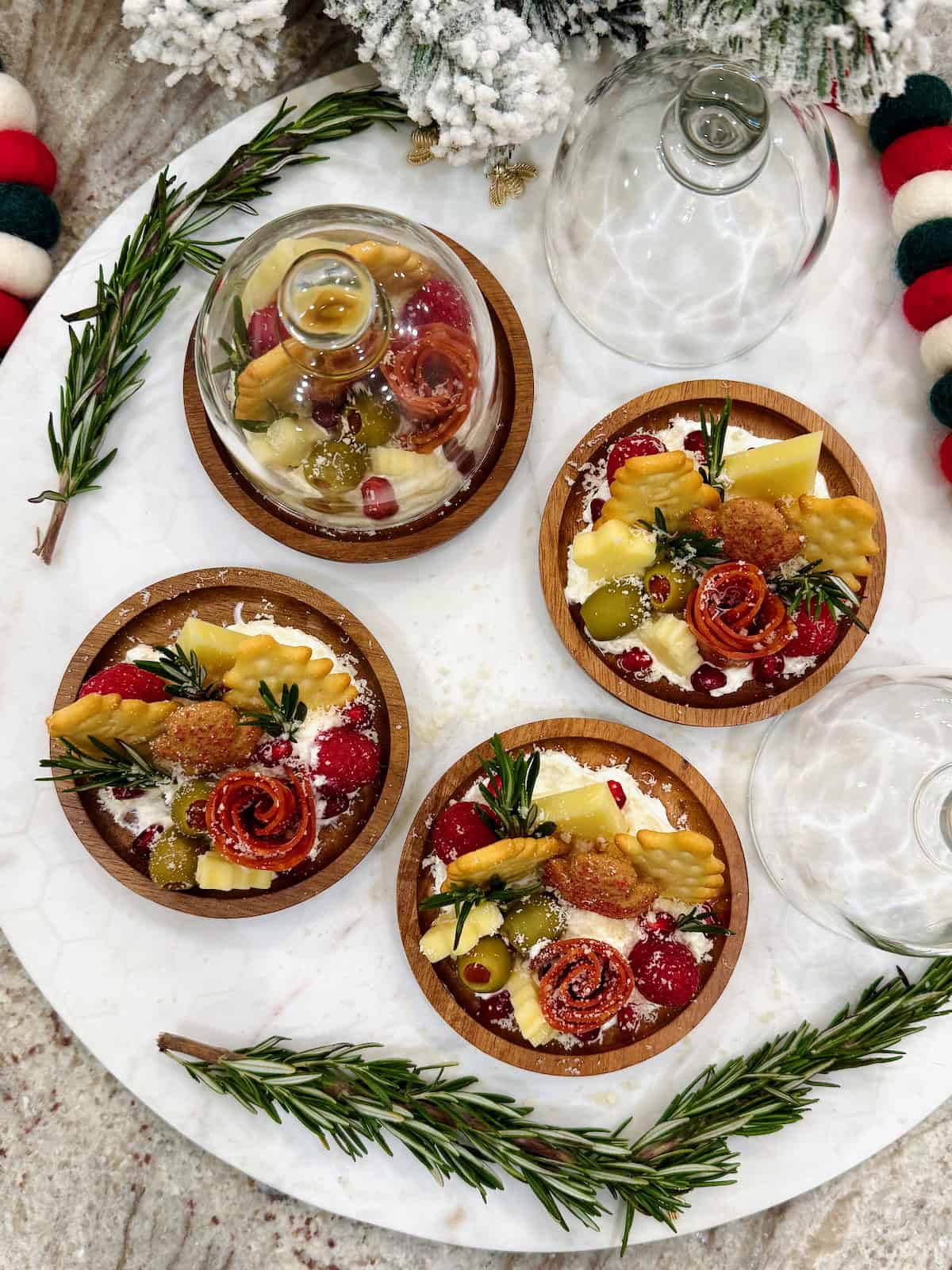 Four small round charcuterie boards feature a salami rose, star cheese and Christmas tree shaped crackers.