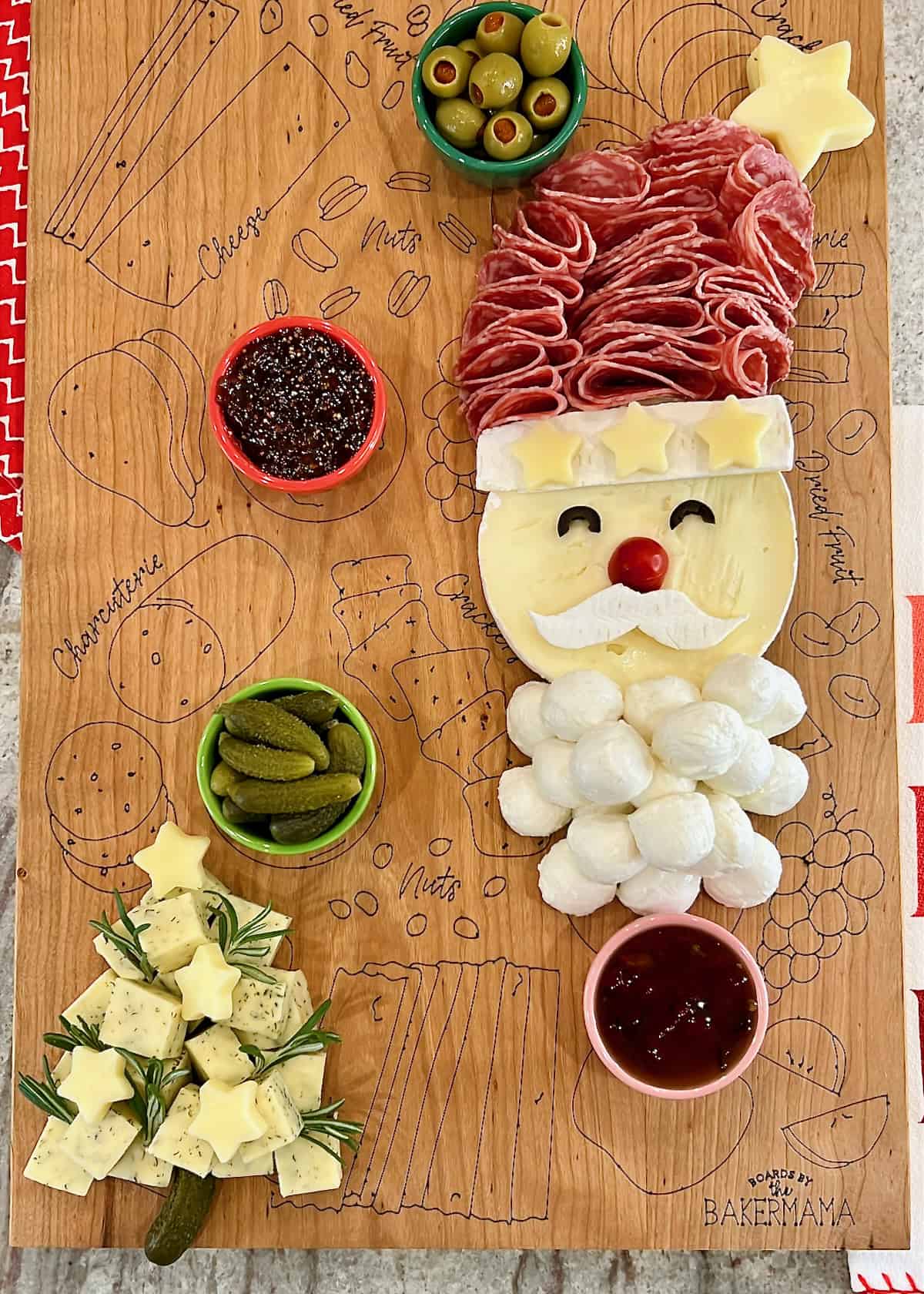 A brie Santa, a cheese Christmas tree and three small bowls on a wooden food board.