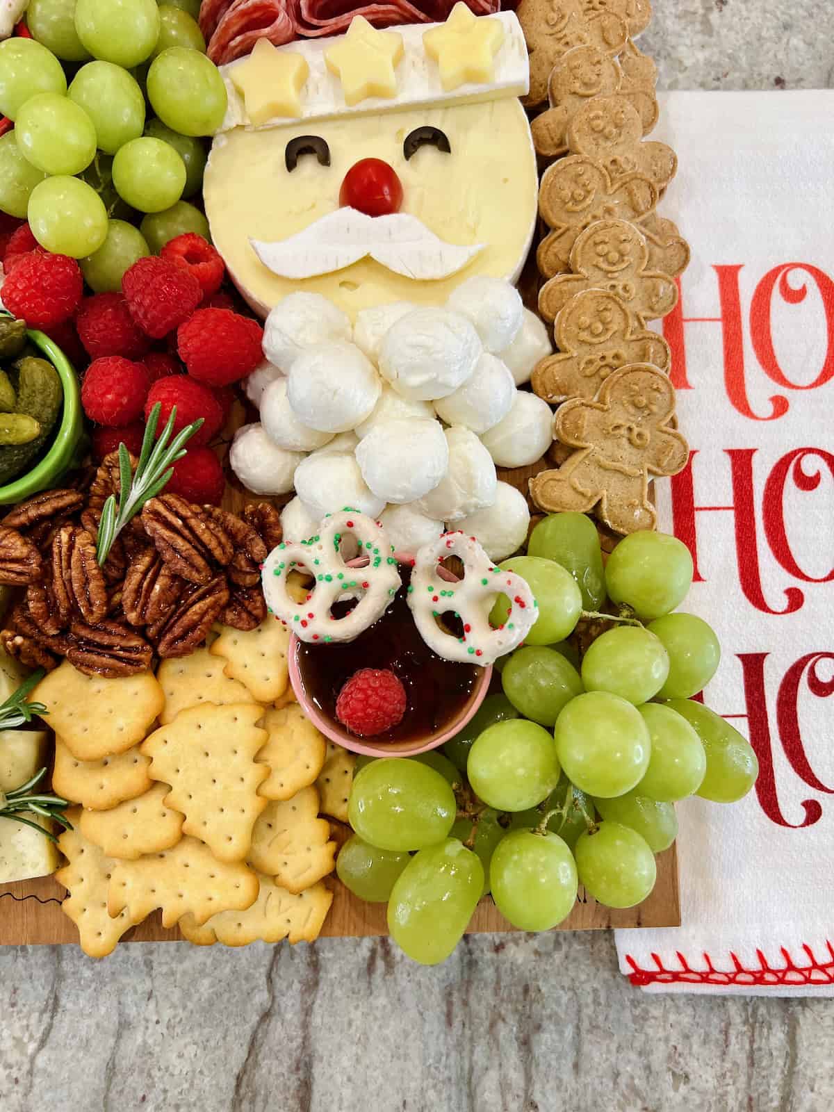 Grapes, Christmas tree shaped crackers, pecan halves and Christmas chocolate covered pretzels on a food board.