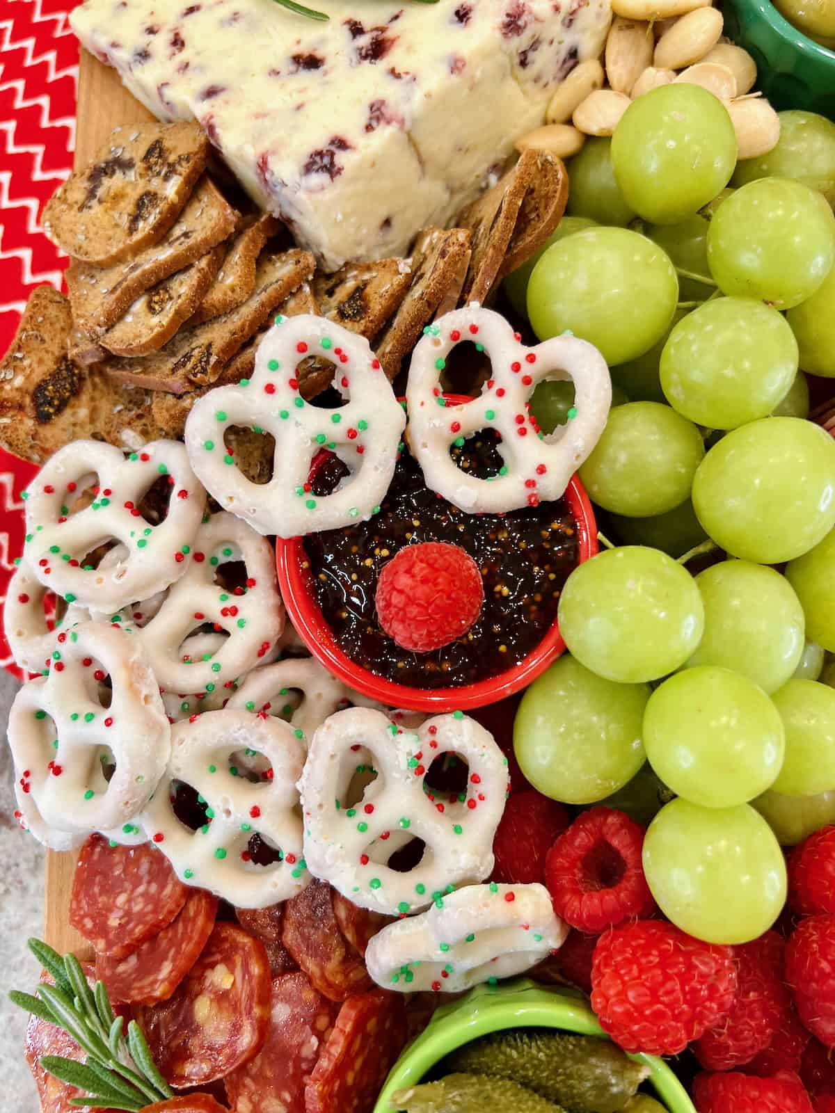 Stilton with cranberries, green grapes, pretzel chips and Christmas chocolate covered pretzels on a charcuterie board.