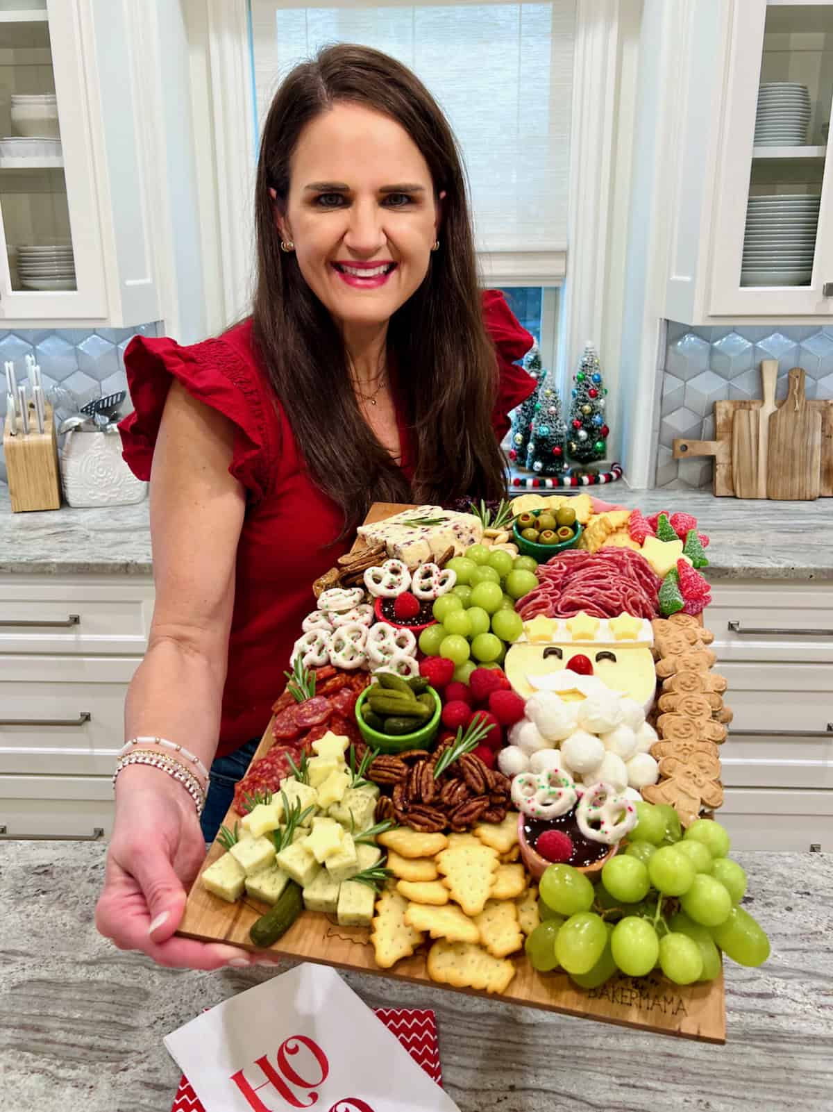 Maegan Brown, wearing a red short sleeve sweater with flutter sleeves, holding a Christmas Santa Signature Board.