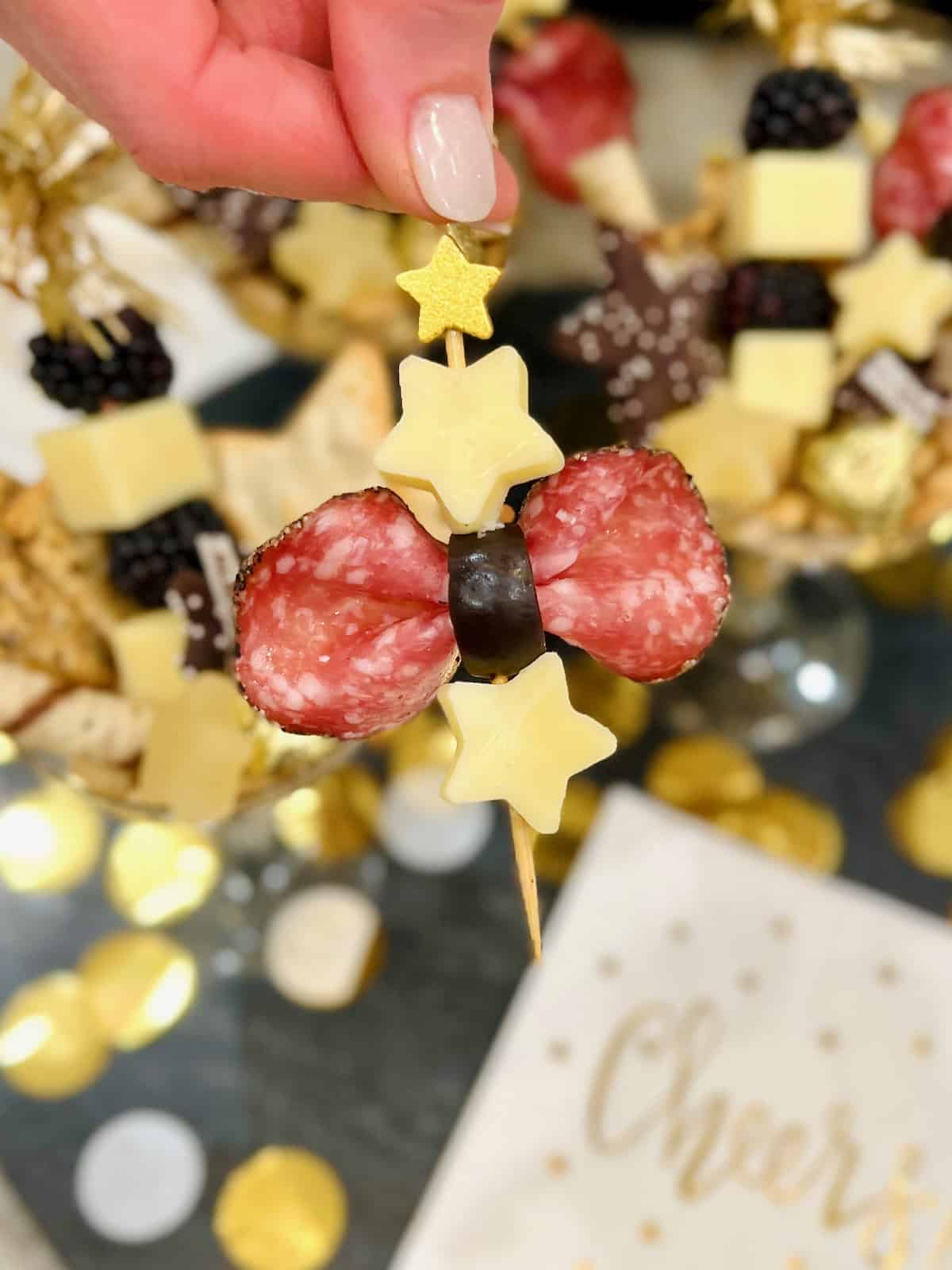 A salami and black olive bow on a skewer with star shaped cheese.