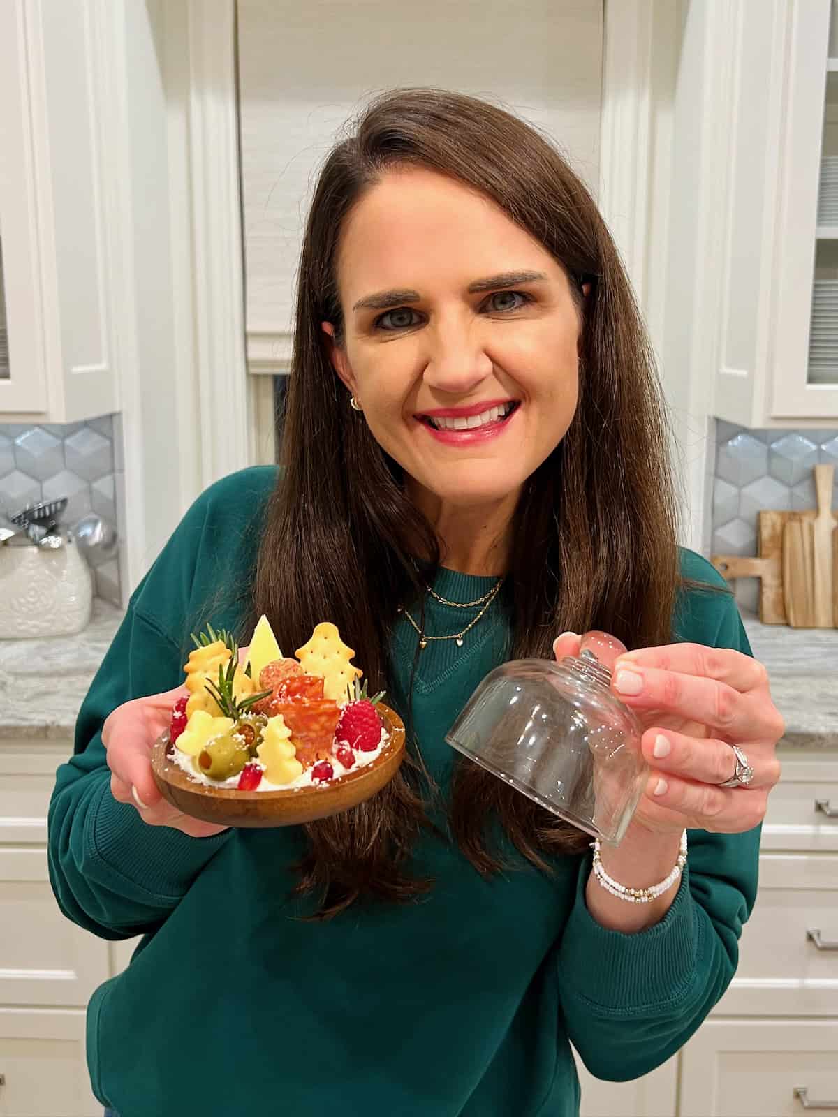 Maegan Brown wearing a dark green sweater holding a Charcuterie Snow Globe.