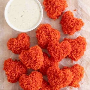 A pile of Flamin' Hot Cheetos Hearts on a white surface next to a small white dish of spicy ranch dressing.