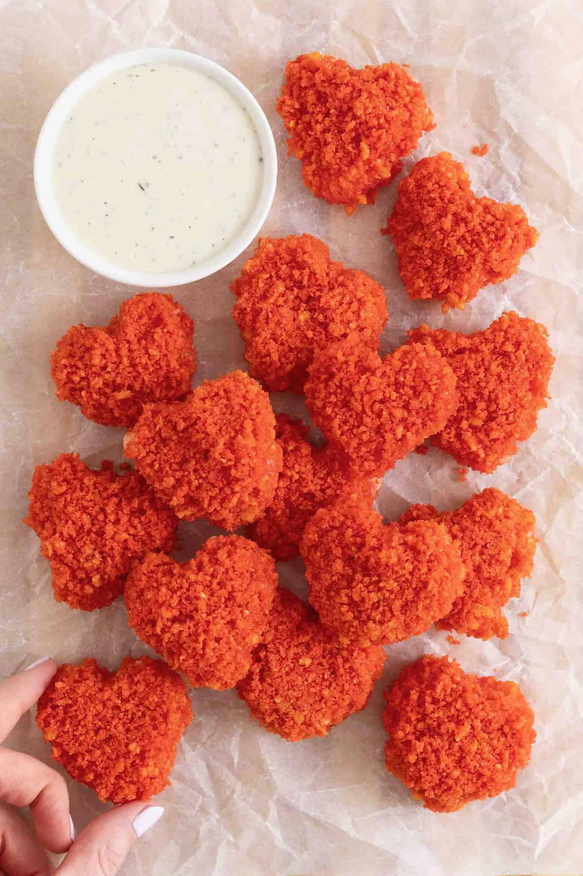A pile of Flamin' Hot Cheeto Hearts on a white surface next to a small white dish of ranch dressing. 