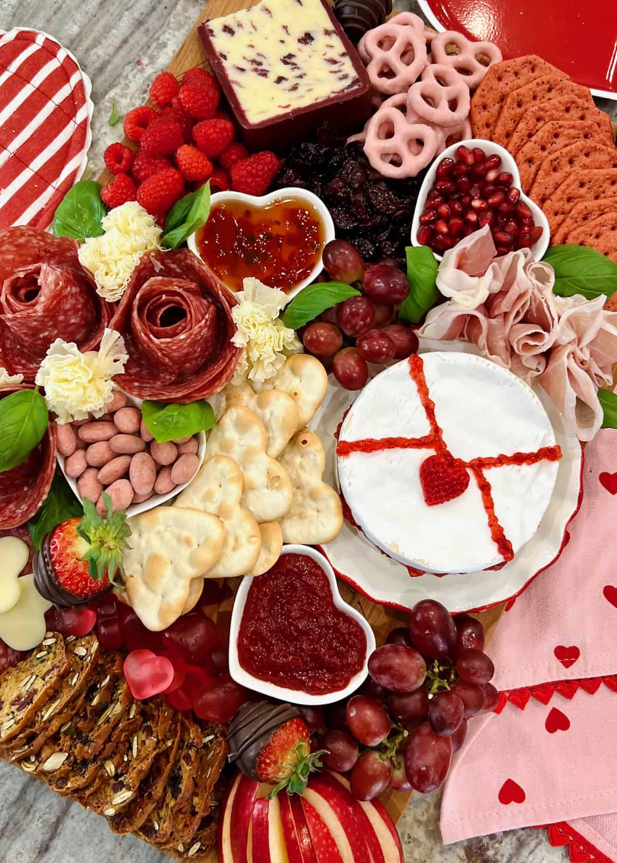 A wood food board decorated with Valentine's Day themed charcuterie items, including a wheel of brie decorated to look like a love letter.