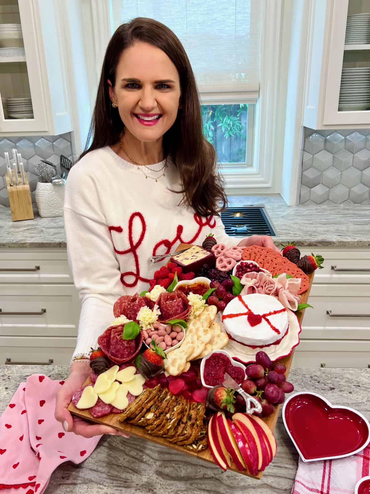 Maegan Brown holding her Valentine's Signature Board. Maegan is wearing a white sweater with the word LOVE written in red cursive.
